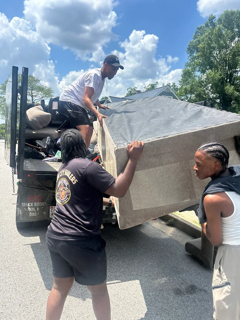 Charm City Haulers crew loading a mattress onto a dump truck in Baltimore